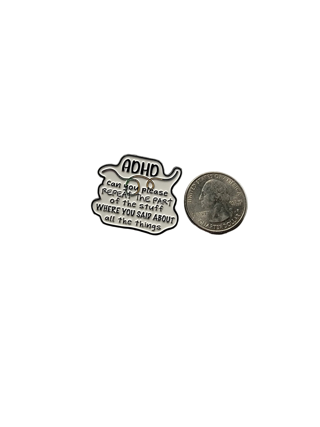Metallic badge with text and a coin for scale on a gray background