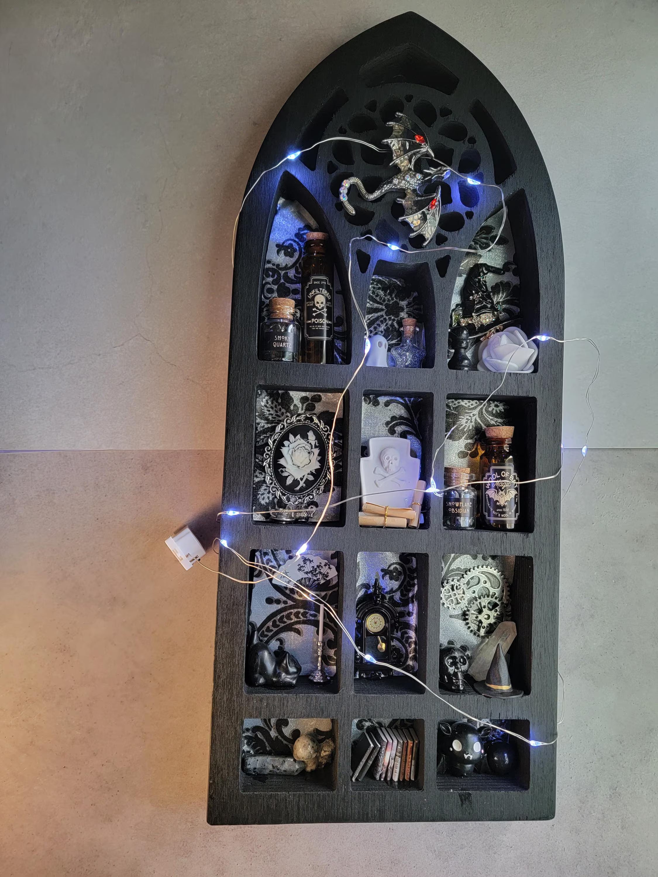 Decorative shelf with small bottles and decorative items inside a gothic arch frame.