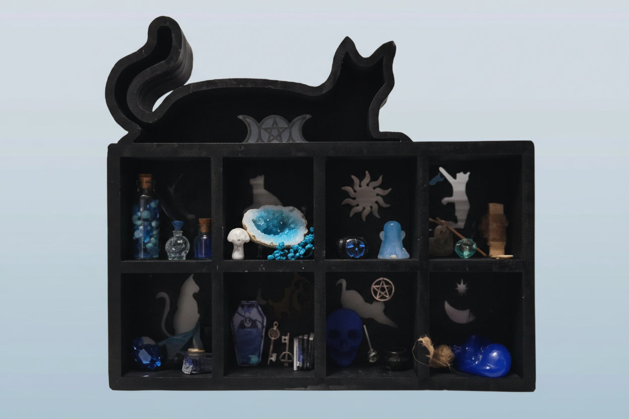 Black cat-shaped jewelry box with compartments containing various small figurines on a light blue background