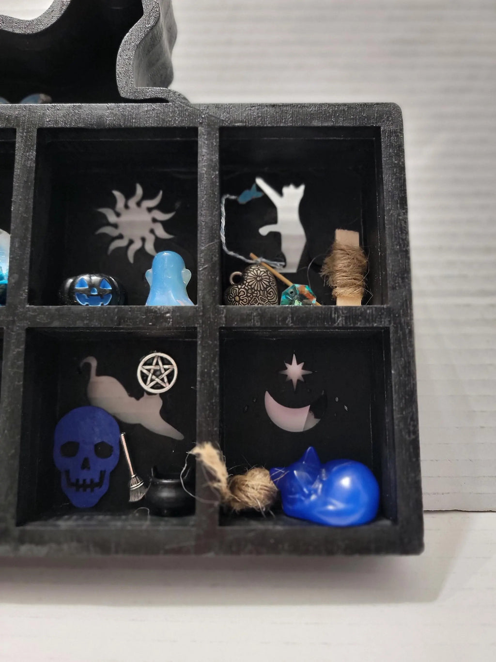 Black shadow box with various small objects including a blue cat figurine, skull, and other decorative items.