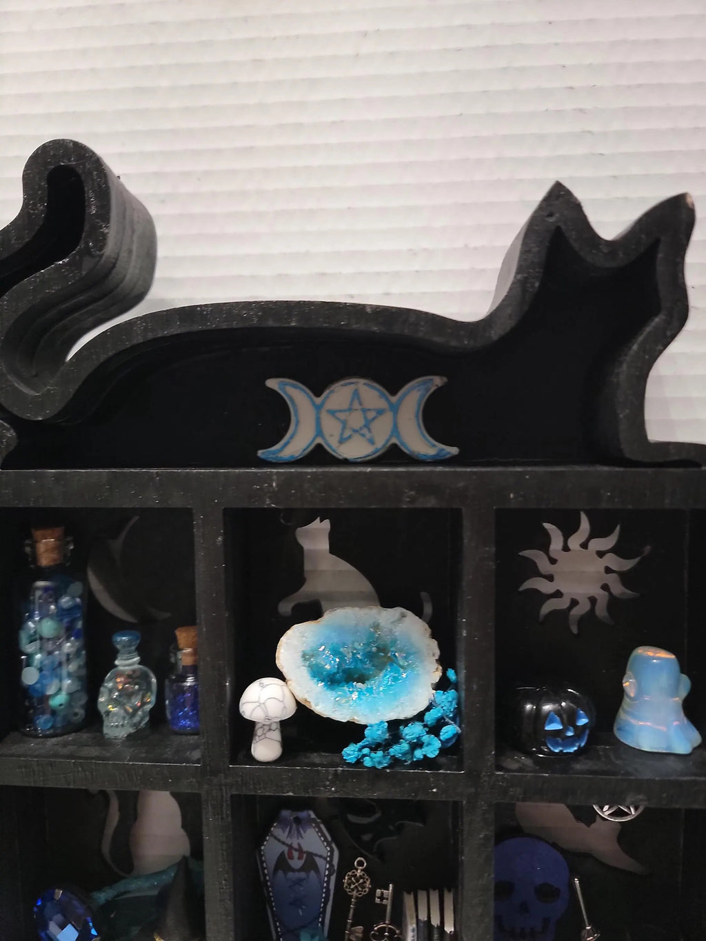 Black stone shelf with decorative items including bottles and a crystal, against a striped wall.