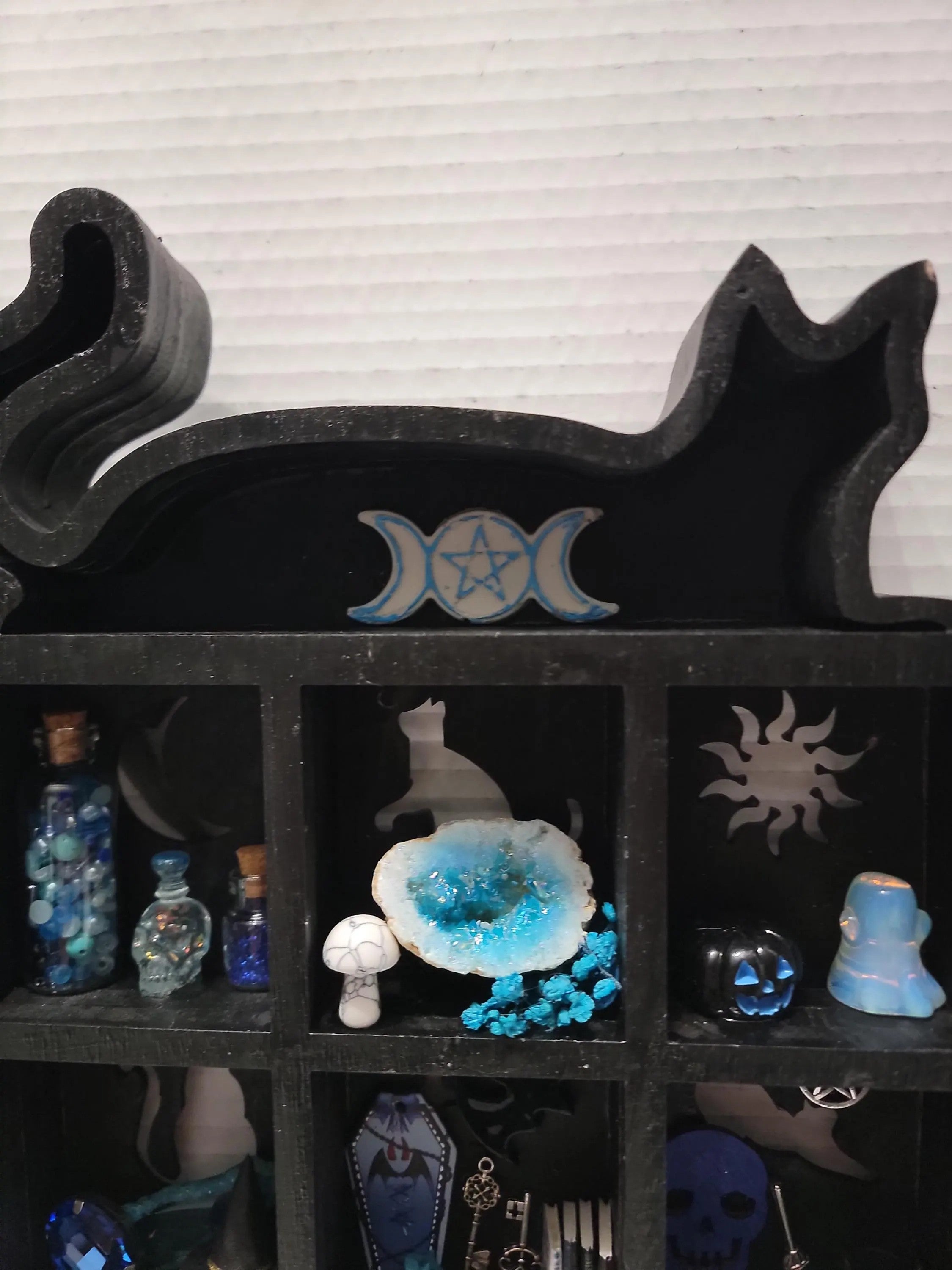 Black stone shelf with decorative items including bottles and a crystal, against a striped wall.