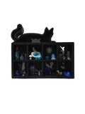 Black display case with various small figurines and objects on a white surface.