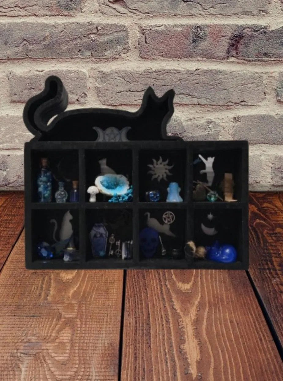 Black cat-shaped black box with small figurines on a wooden surface and brick wall background