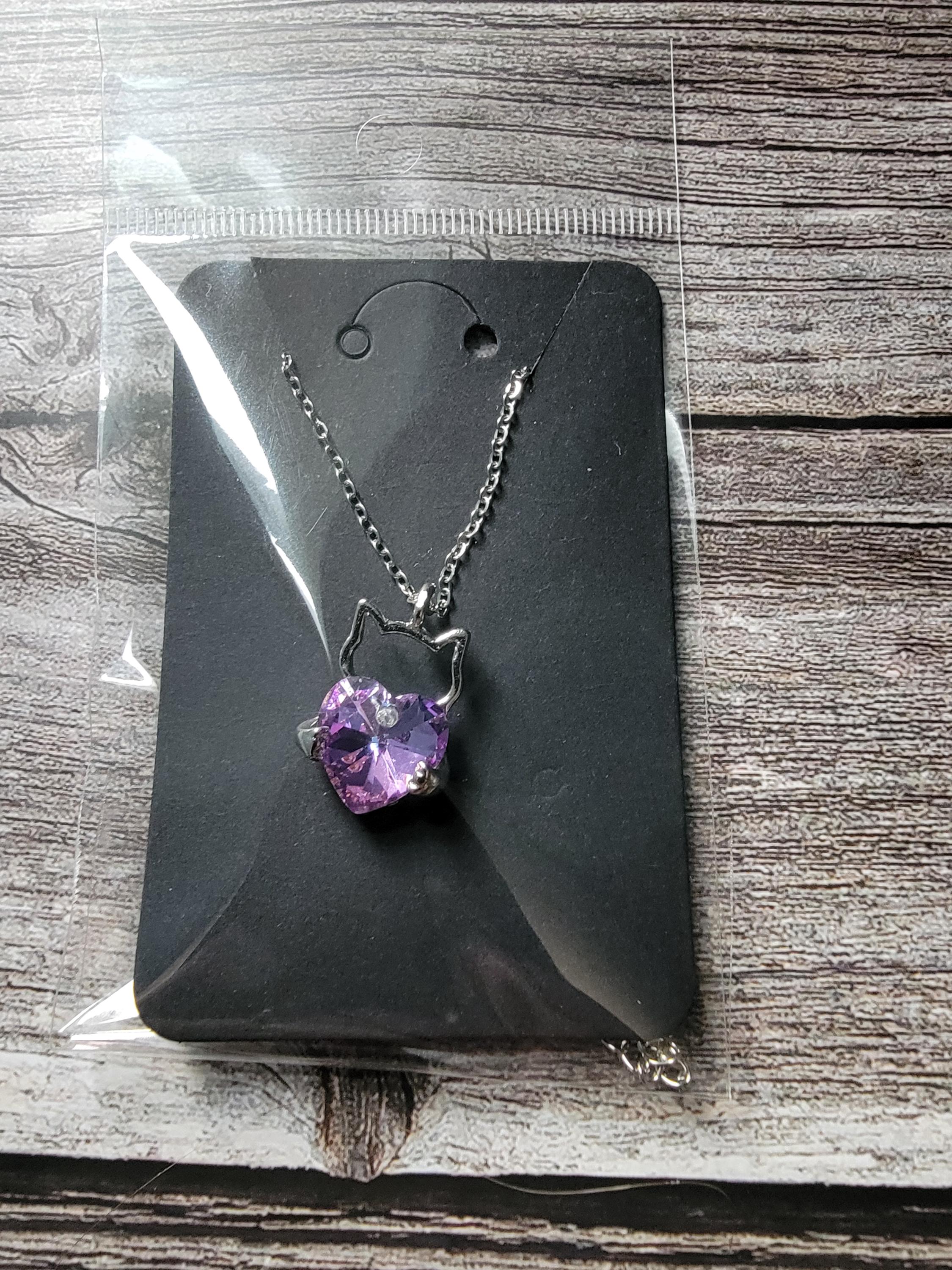 Necklace with a purple pendant on a black card, placed on a wooden surface.