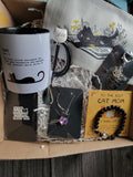 Cat-themed gift set with mug, necklace, and bracelet in a box.