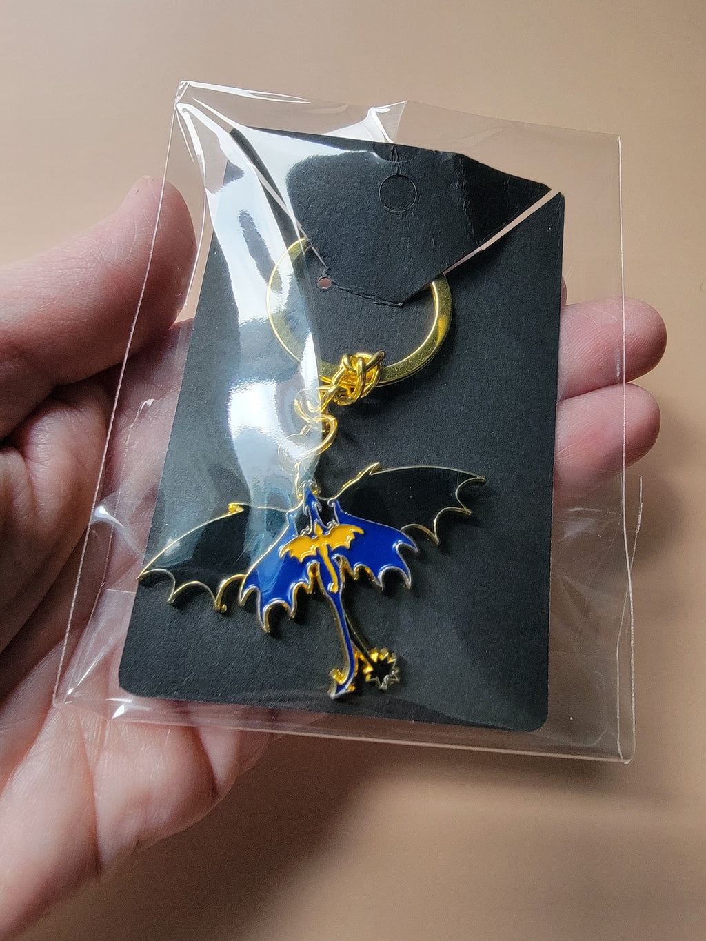 Dragon-shaped keychain with blue and gold design on a clear card held by a hand.