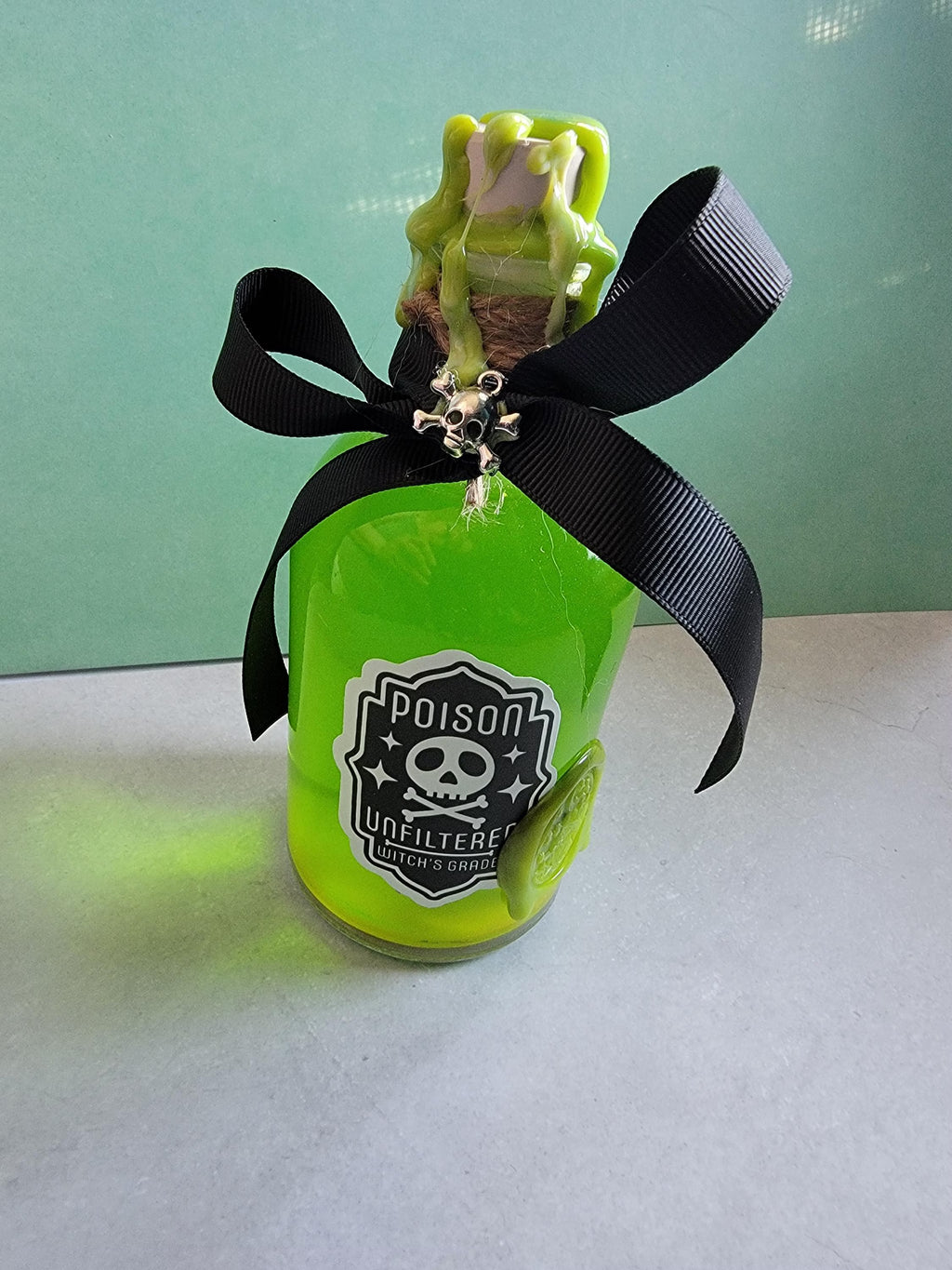 Neon green bottle with a black ribbon and frog figure on a light gray surface.
