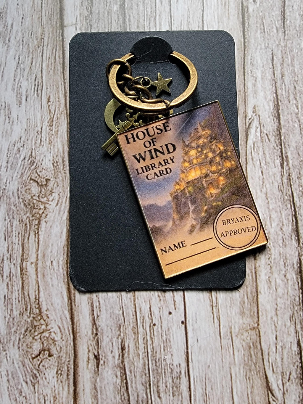 Decorative keychain with 'House of Wind' library card design on a wooden surface