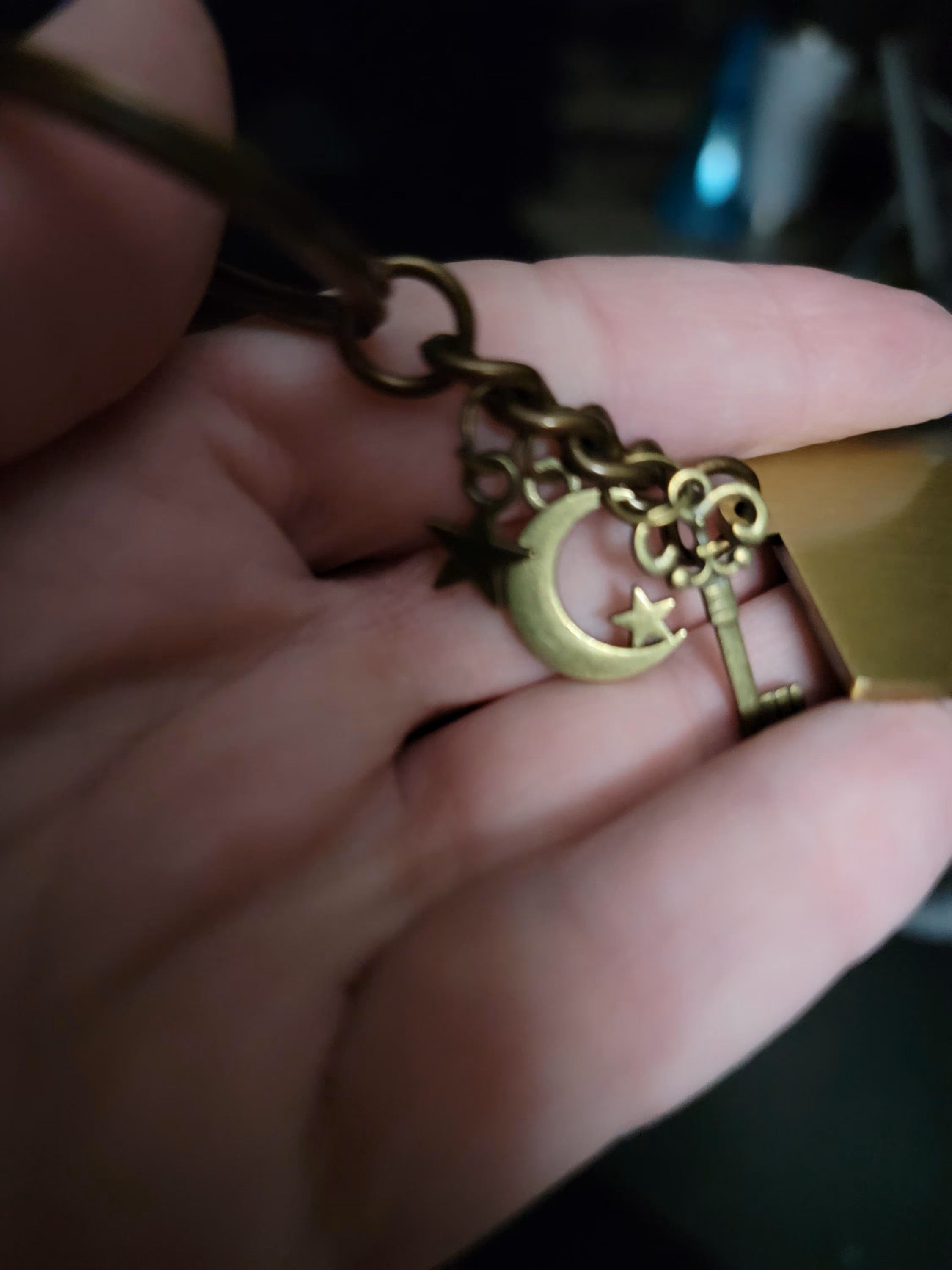 Hand holding a brass key-shaped pendant with a moon and star design.
