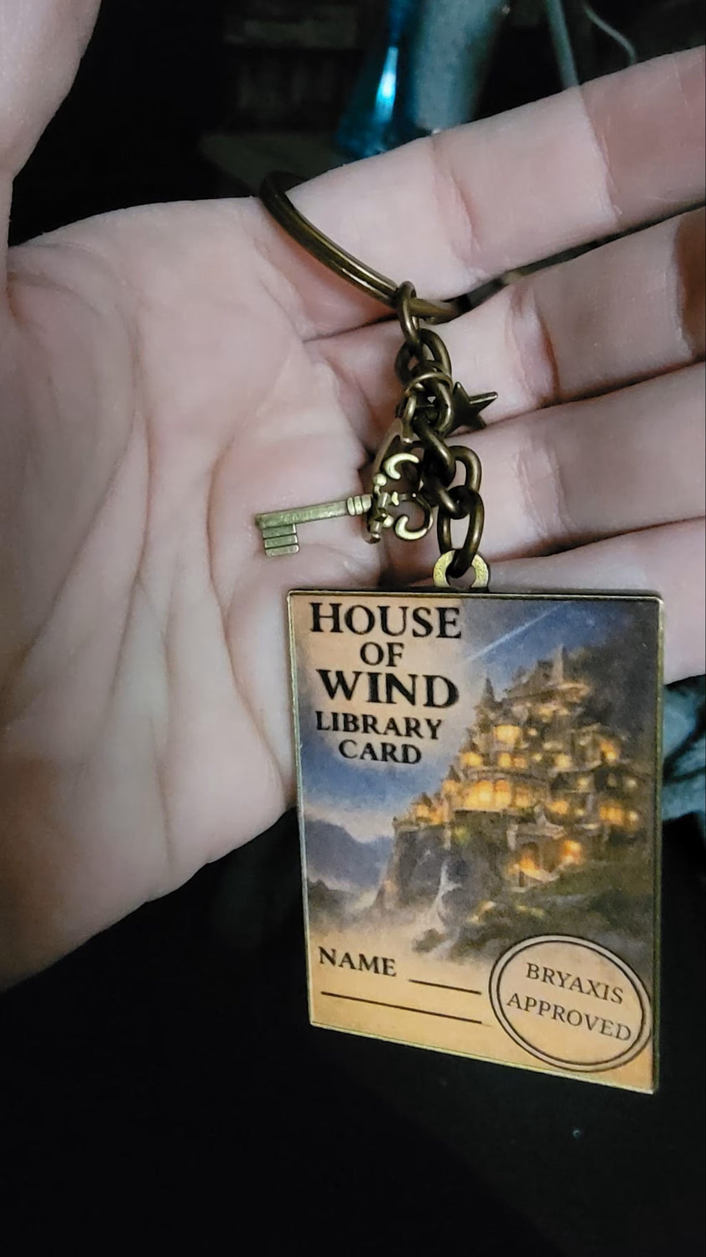 Keychain with 'House of Wind Library Card' design on a hand