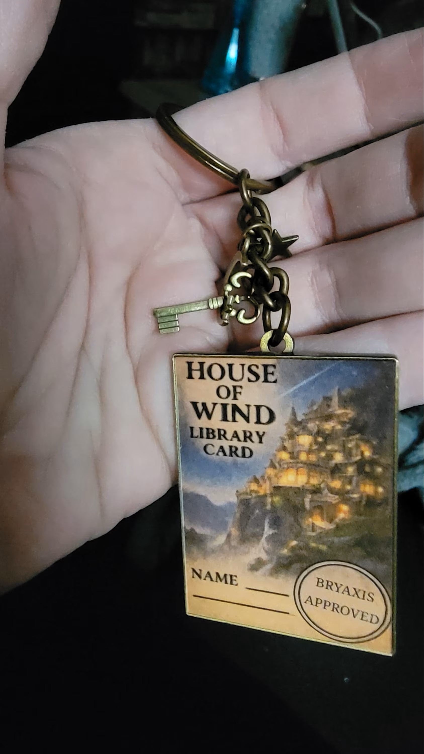 Keychain with 'House of Wind Library Card' design on a hand