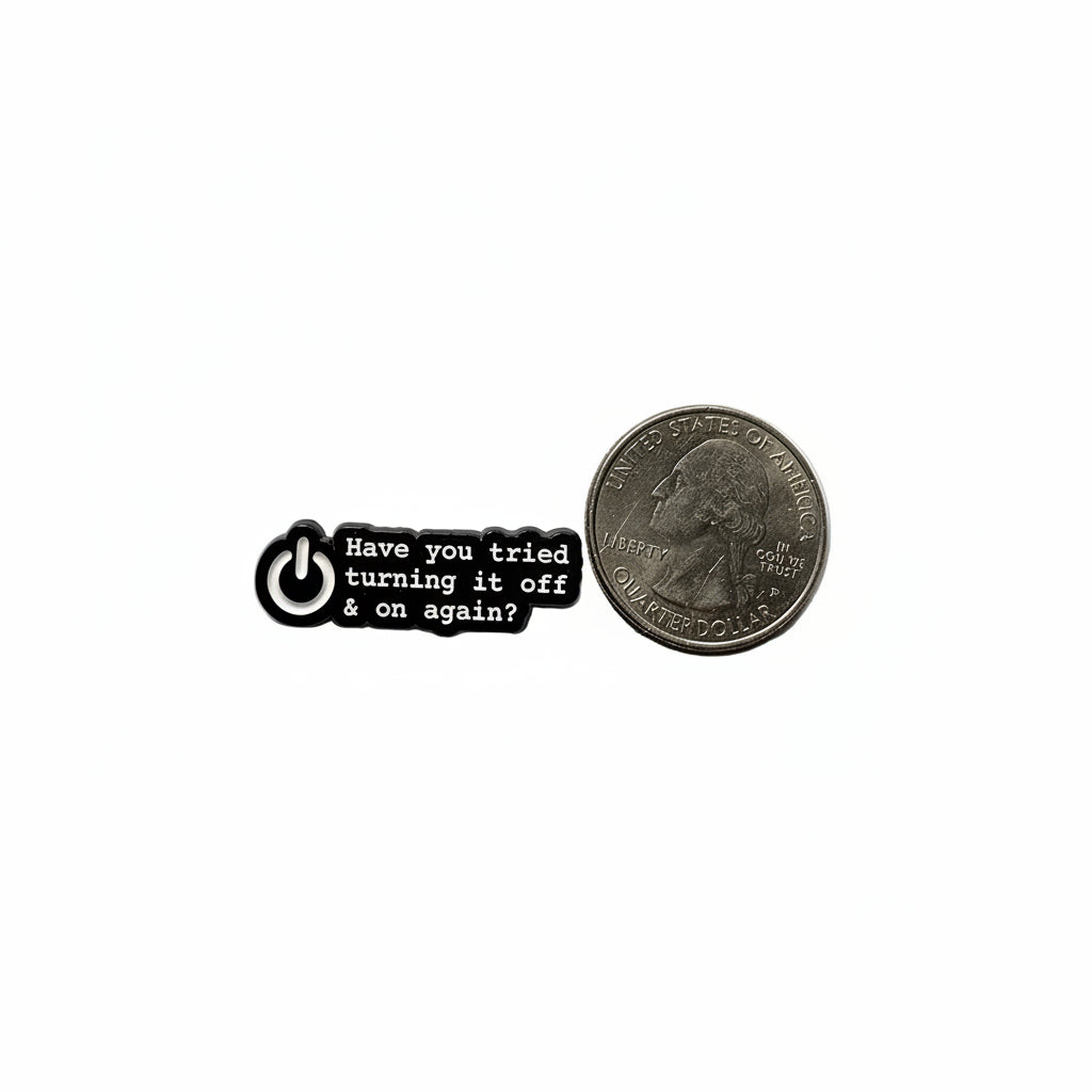 Small black and white pin with text next to an American quarter on a white background