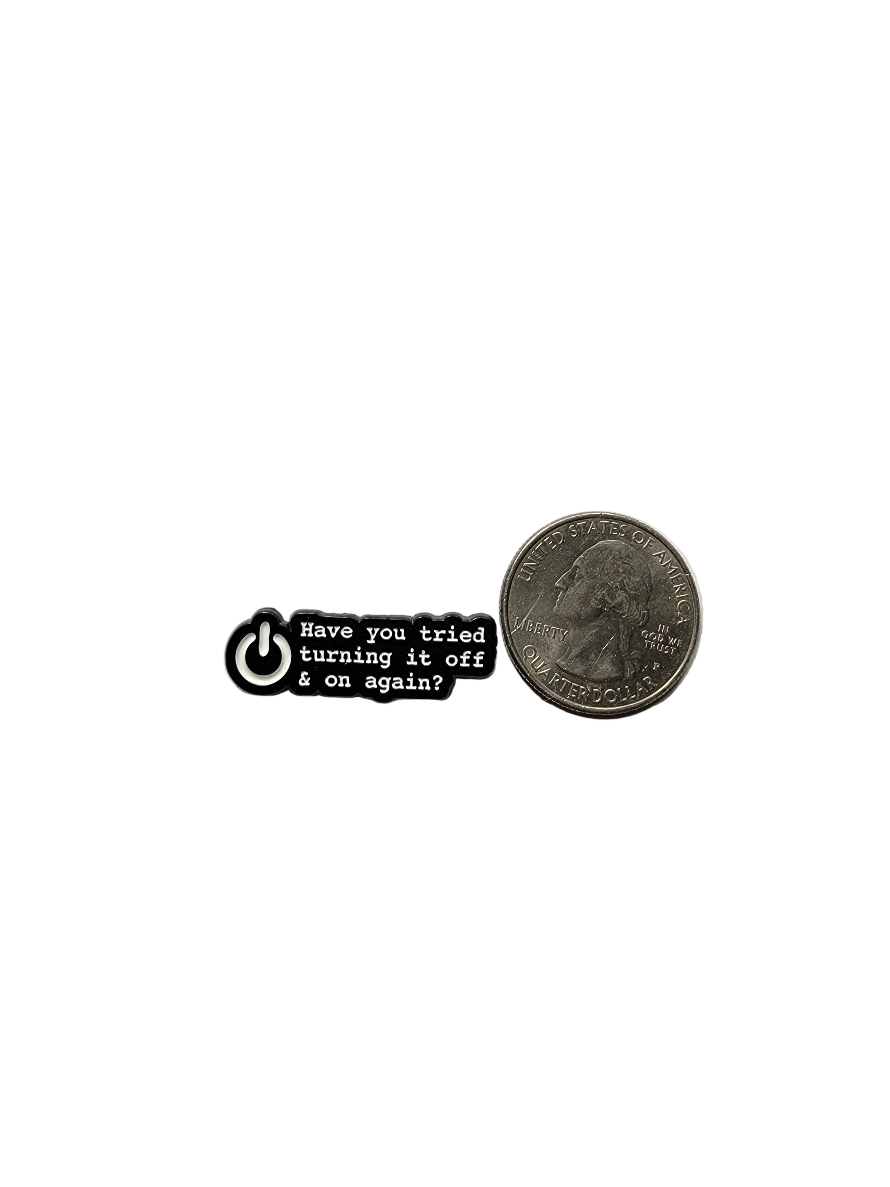 Small black and white pin with text next to an American quarter on a white background
