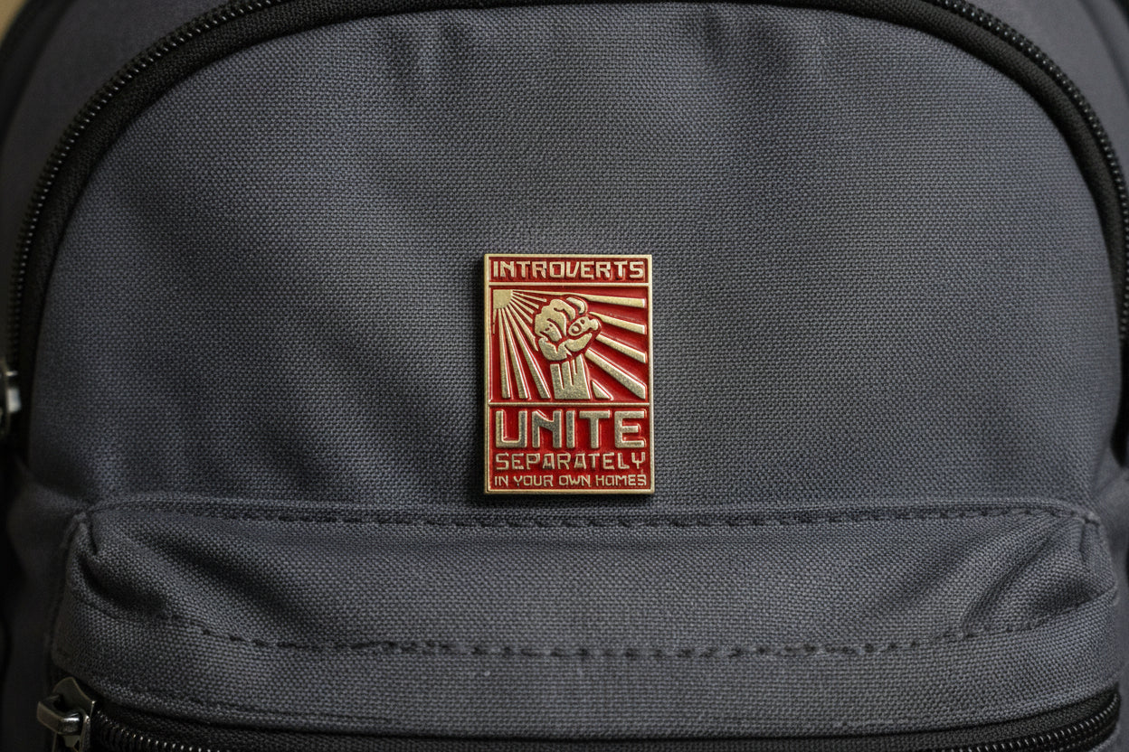 Metallic pin with text on a light gray backpack
