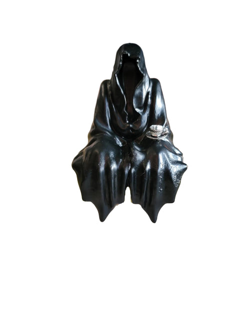 Black cloaked figure sitting down with a teacup on a white background