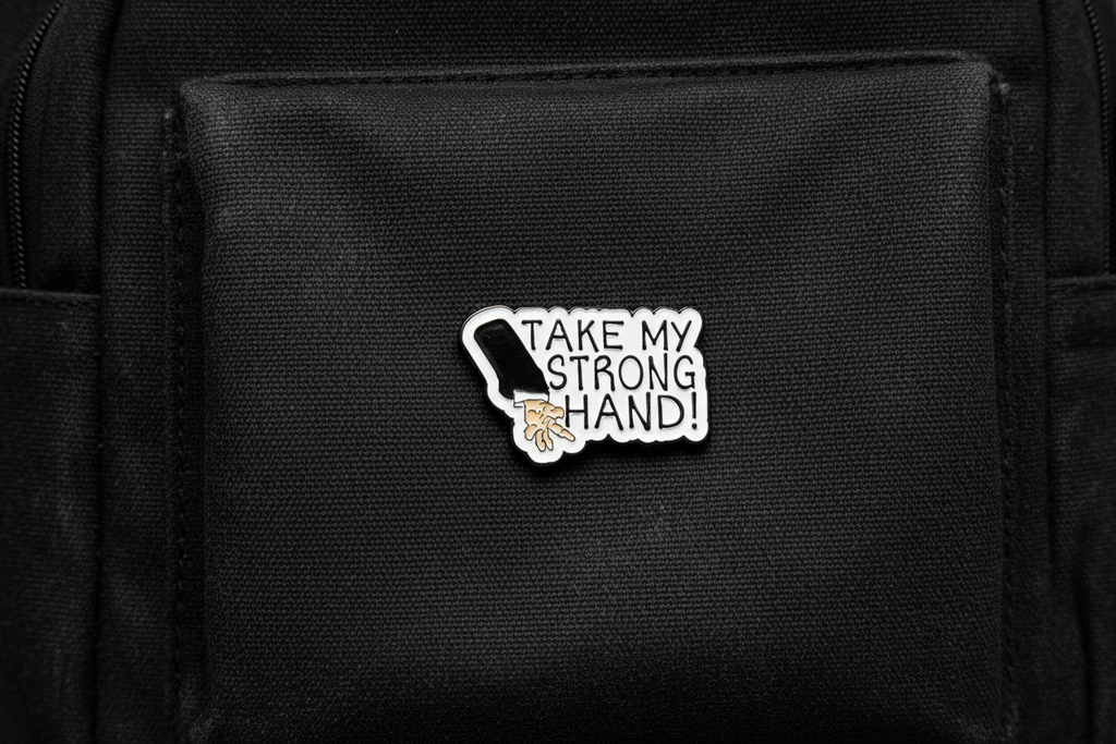 Pin with a design of a hand and text 'Take my strong hand' on a black fabric background