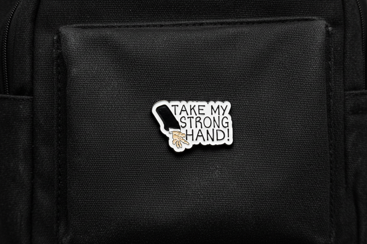 Pin with a design of a hand and text 'Take my strong hand' on a black fabric background