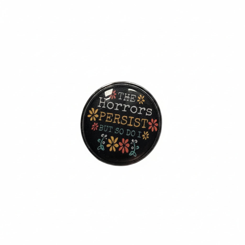 Round black pin with text and floral designs on a light gray background