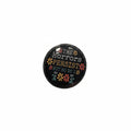 Round black pin with text and floral designs on a light gray background