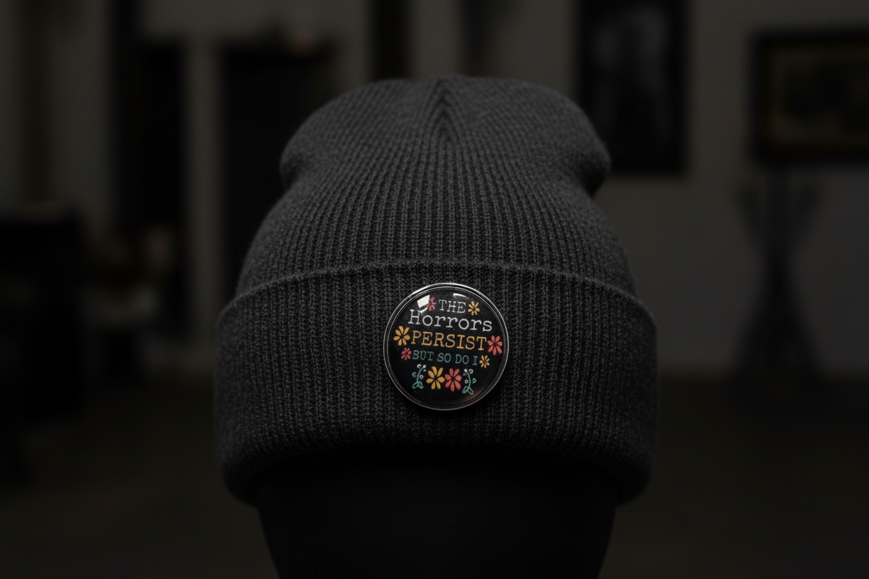 Round black pin with text and floral designs on a black beanie background