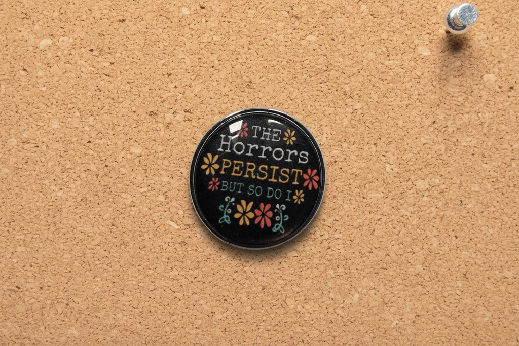 Round black pin with text and floral designs on a cork background