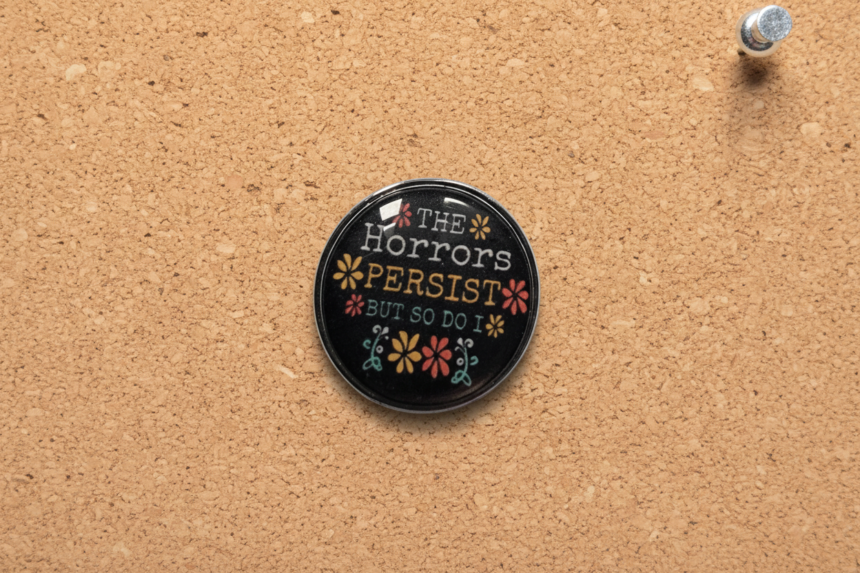 Round black pin with text and floral designs on a cork background