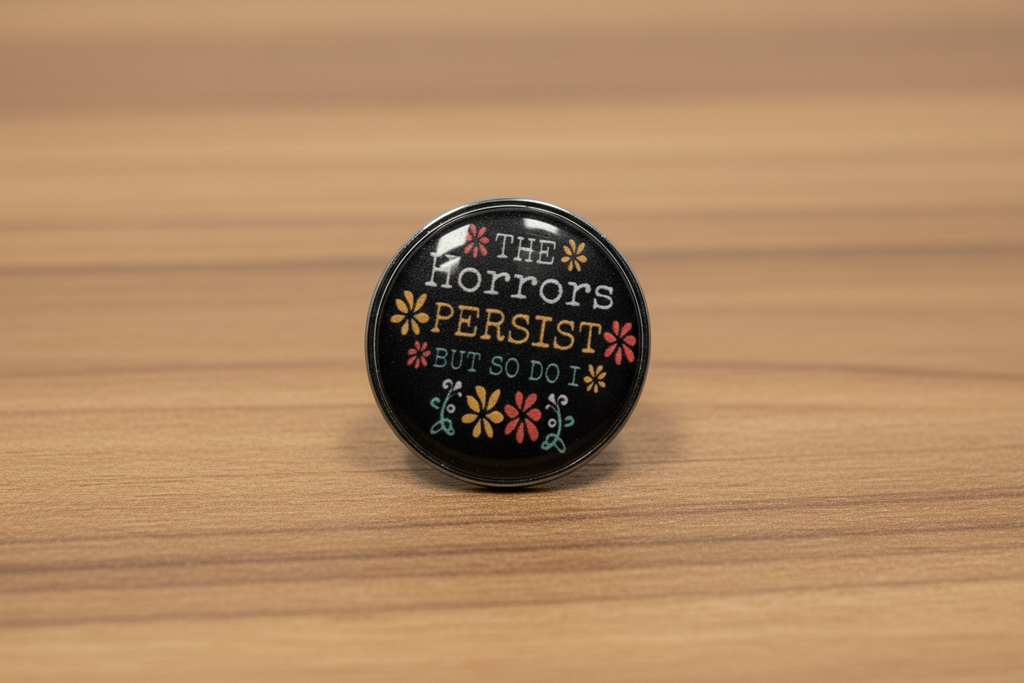 Round black pin with text and floral designs on a wood background