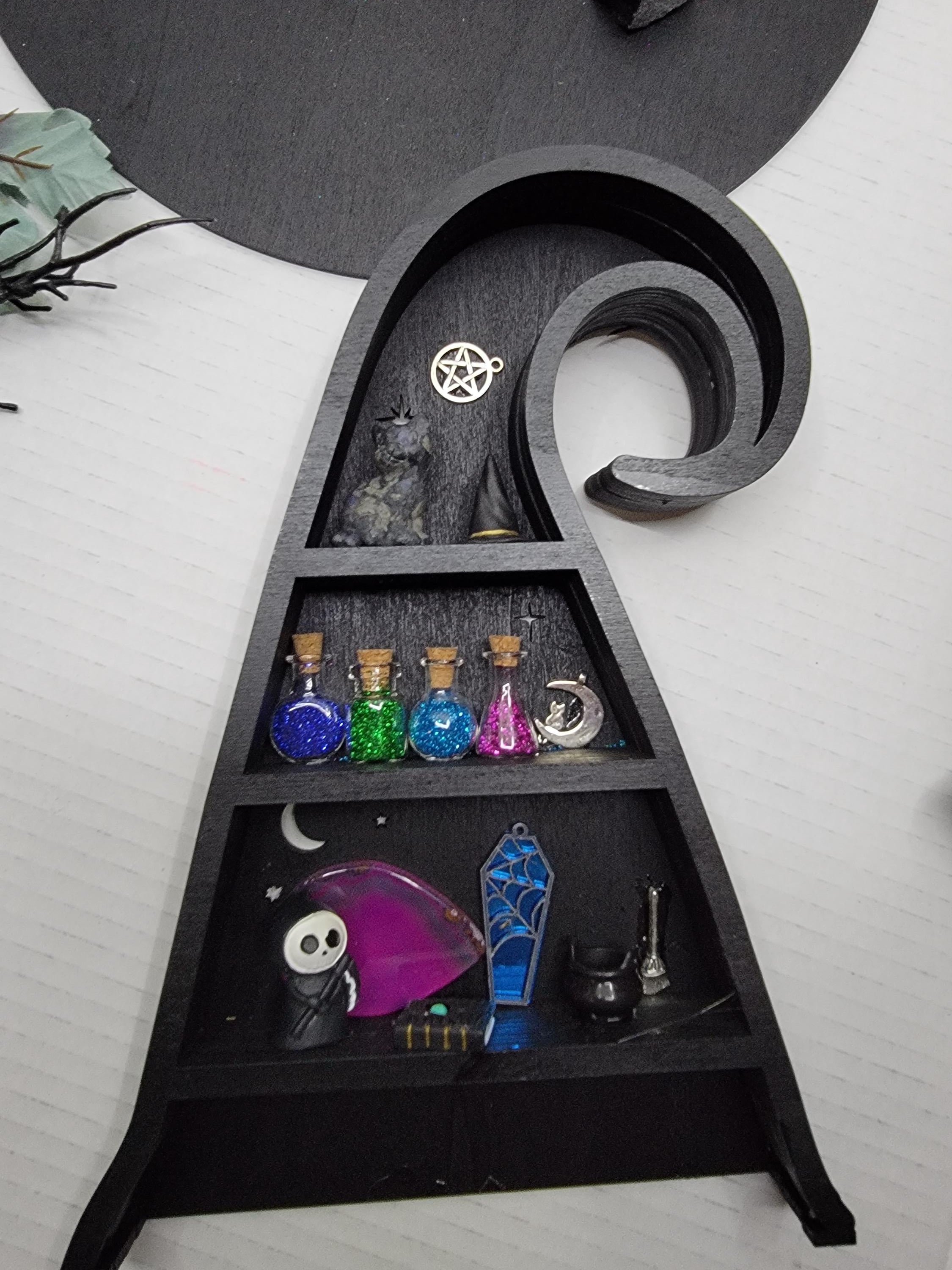 Black witch hat display with compartments containing various small items on a white surface.