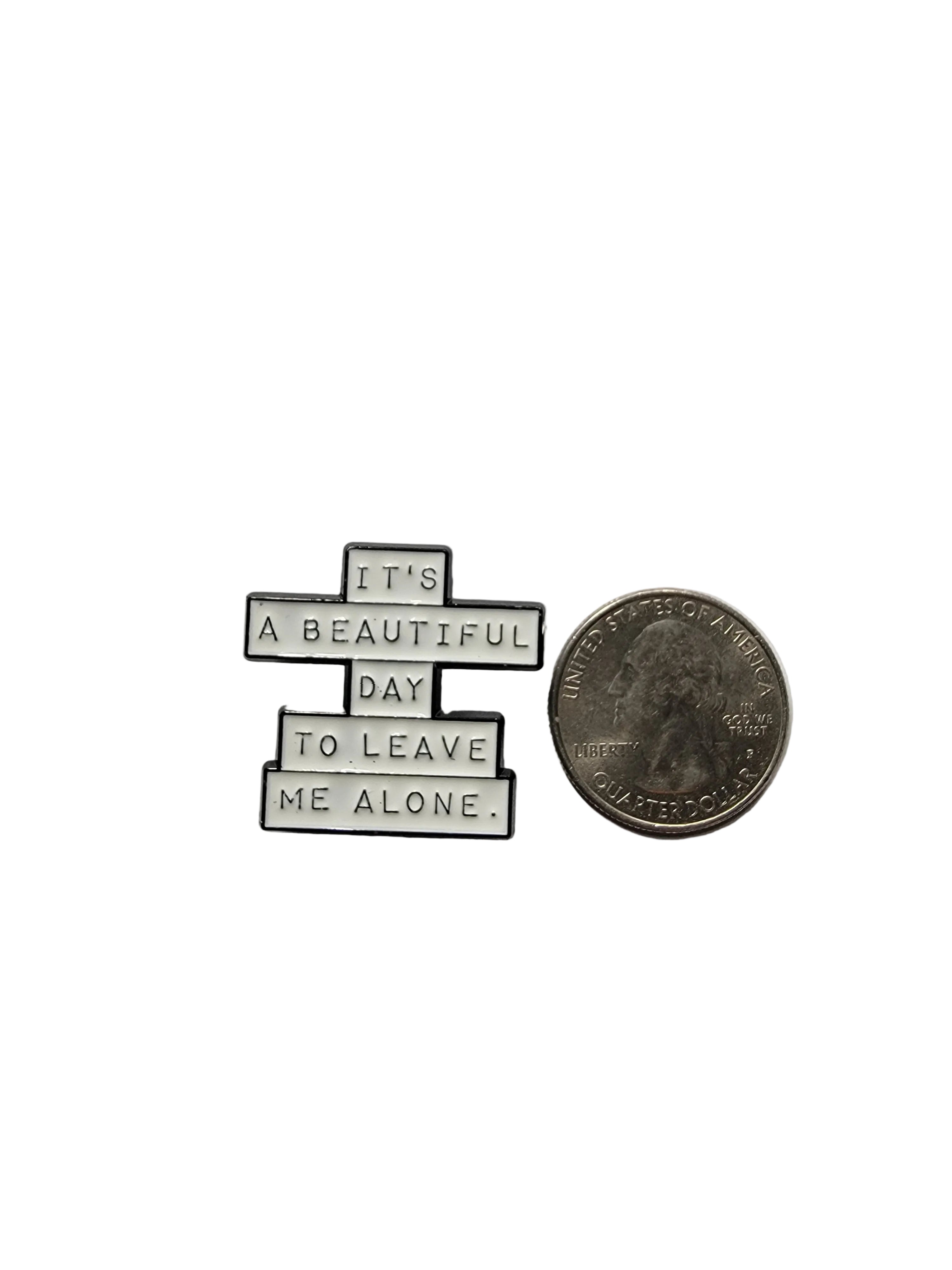 Small metal art piece with text next to a quarter on a gray background