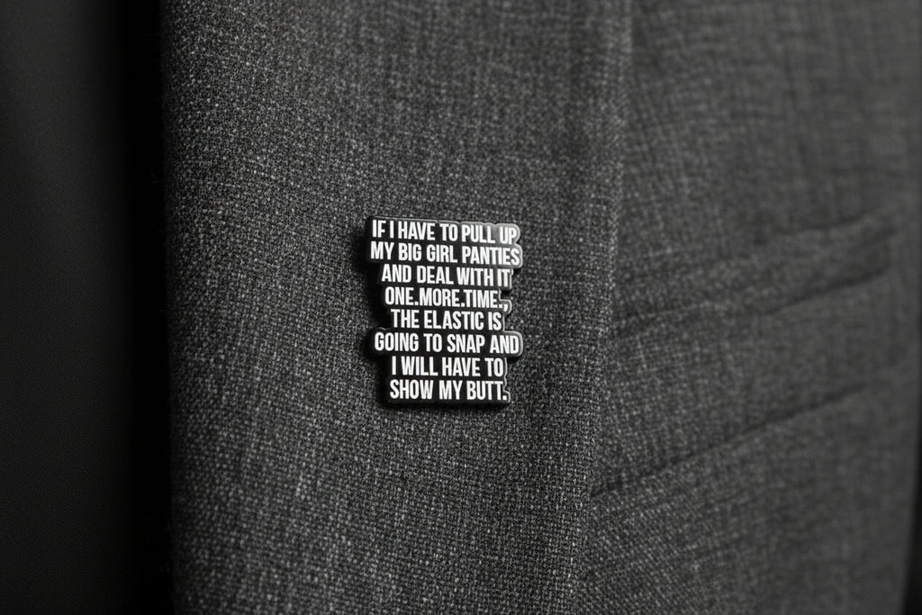 a black enamel pin with white text next to a quarter on a gray fabric background