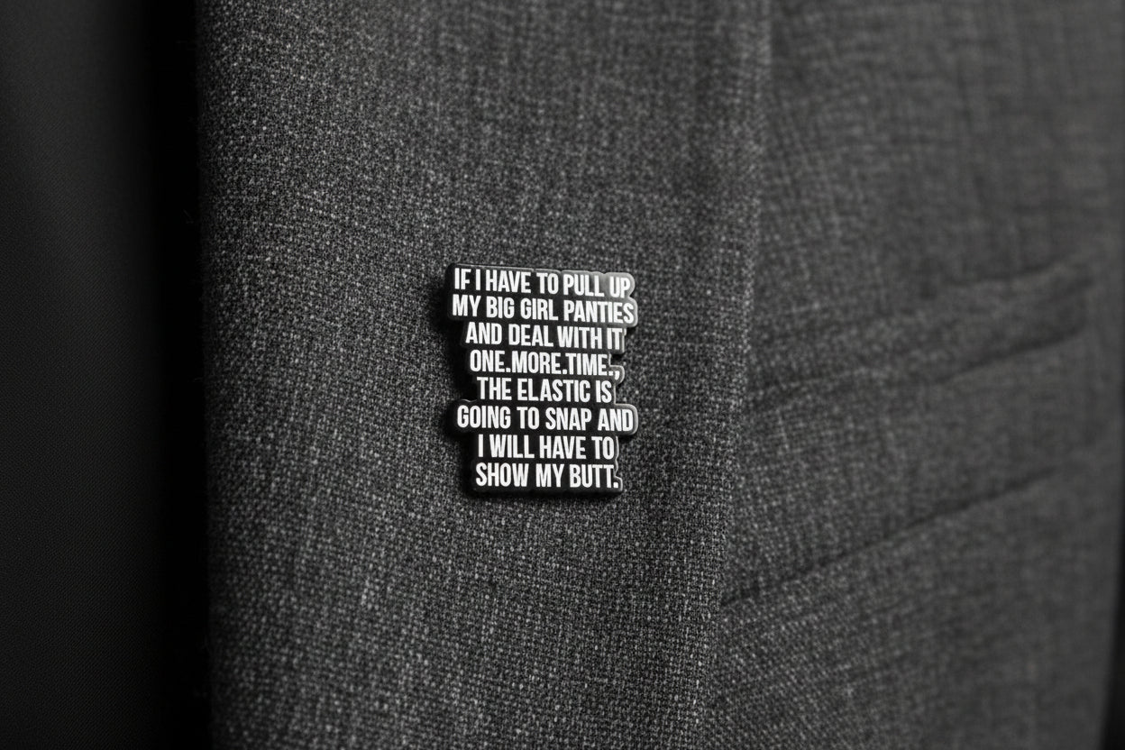 a black enamel pin with white text next to a quarter on a gray fabric background