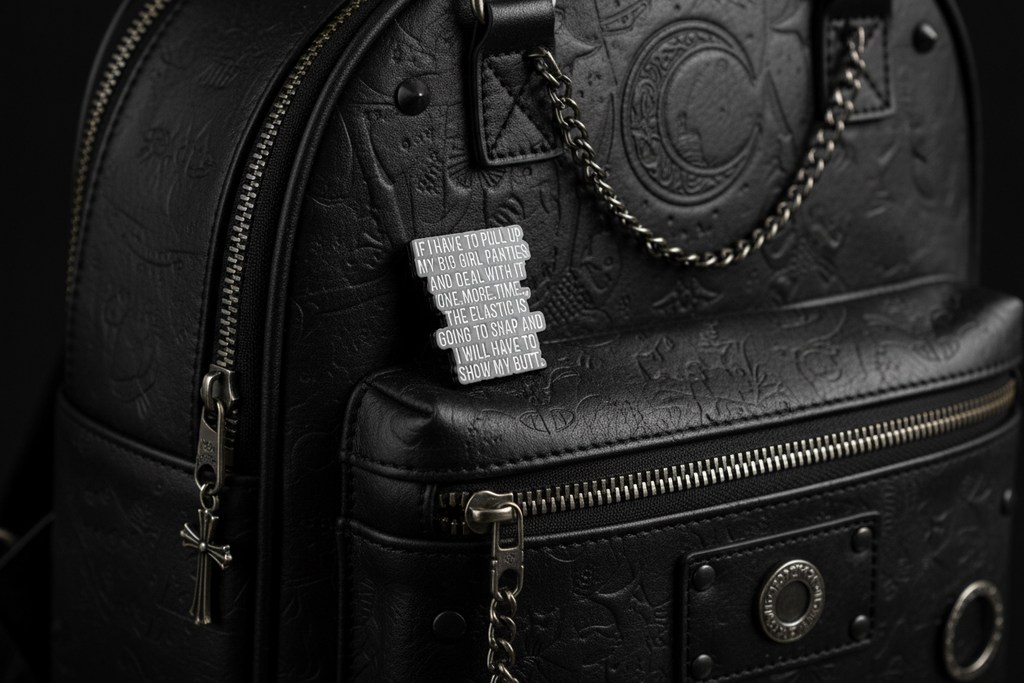 a black enamel pin with white text on a black bookbag background