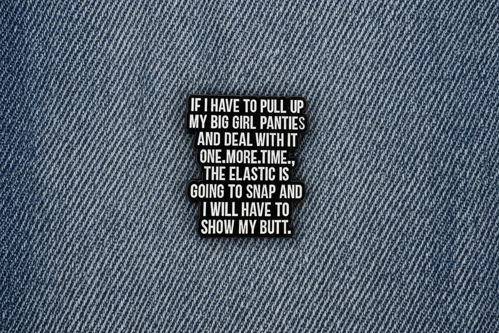 a black enamel pin with white text on a denim background