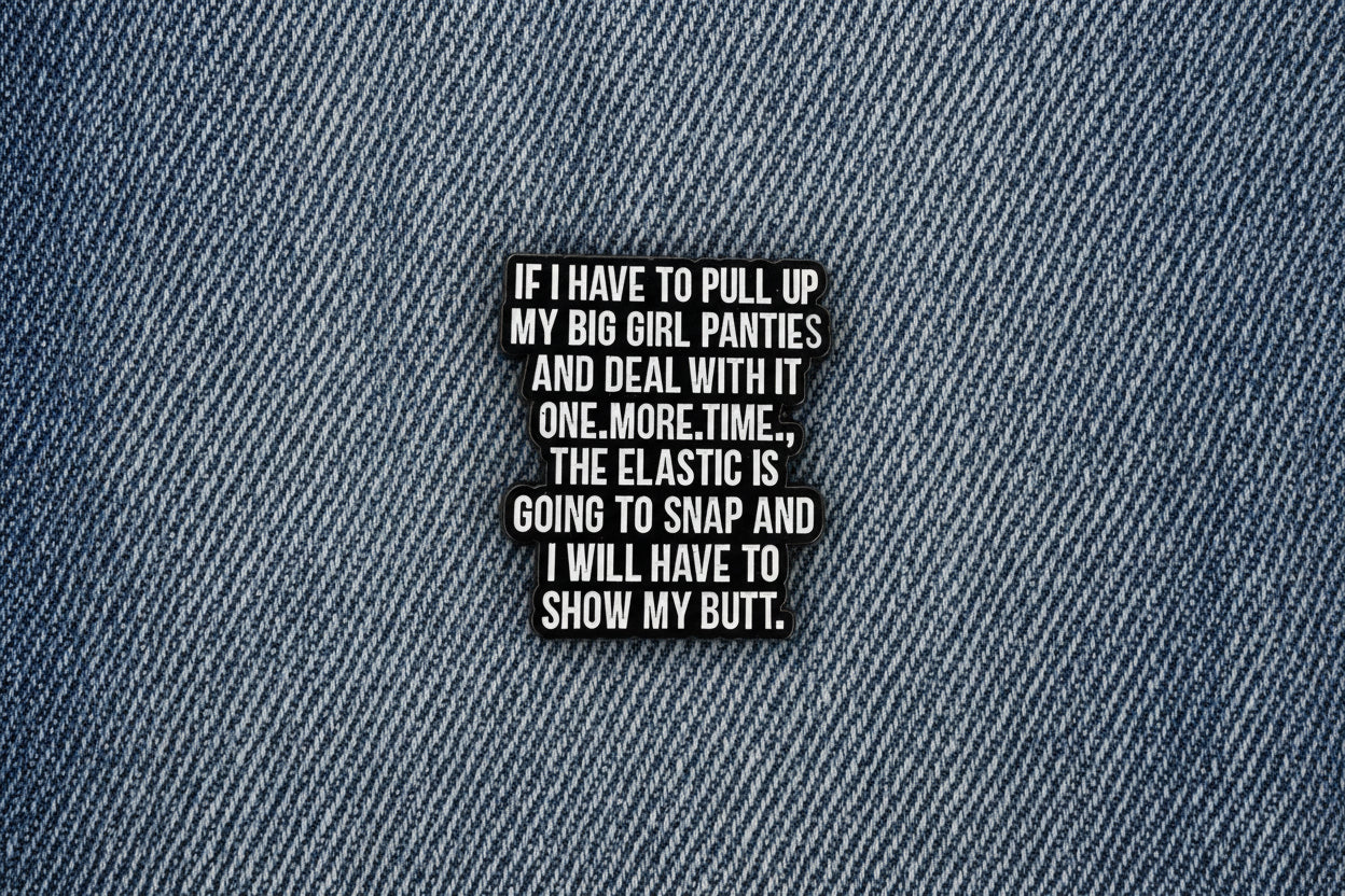 a black enamel pin with white text on a denim background