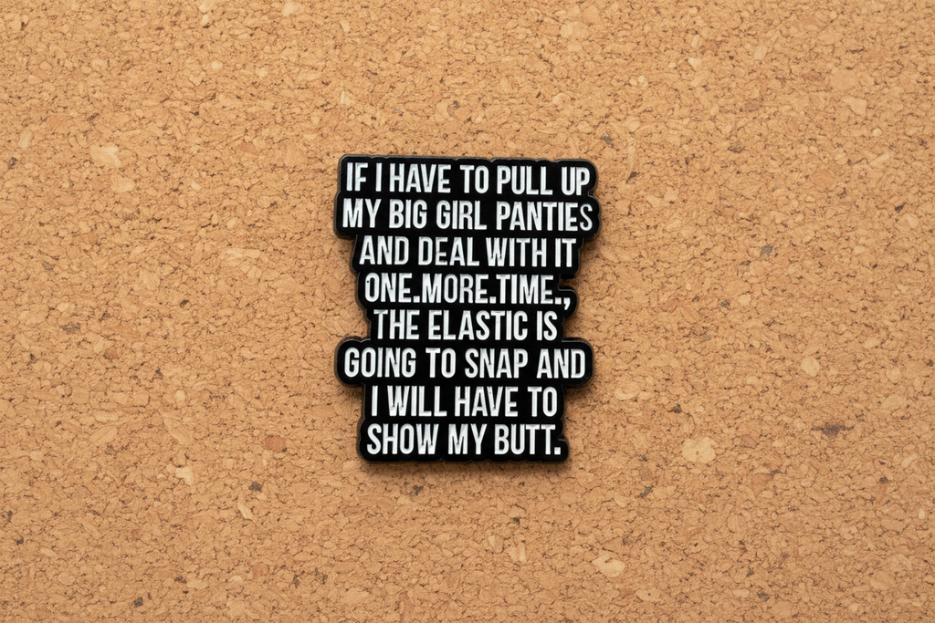 a black enamel pin with white text on a cork background
