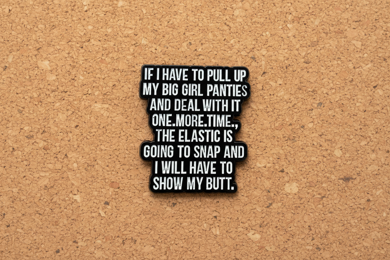 a black enamel pin with white text on a cork background