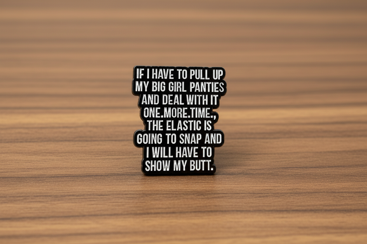 a black enamel pin with white text on a wood background