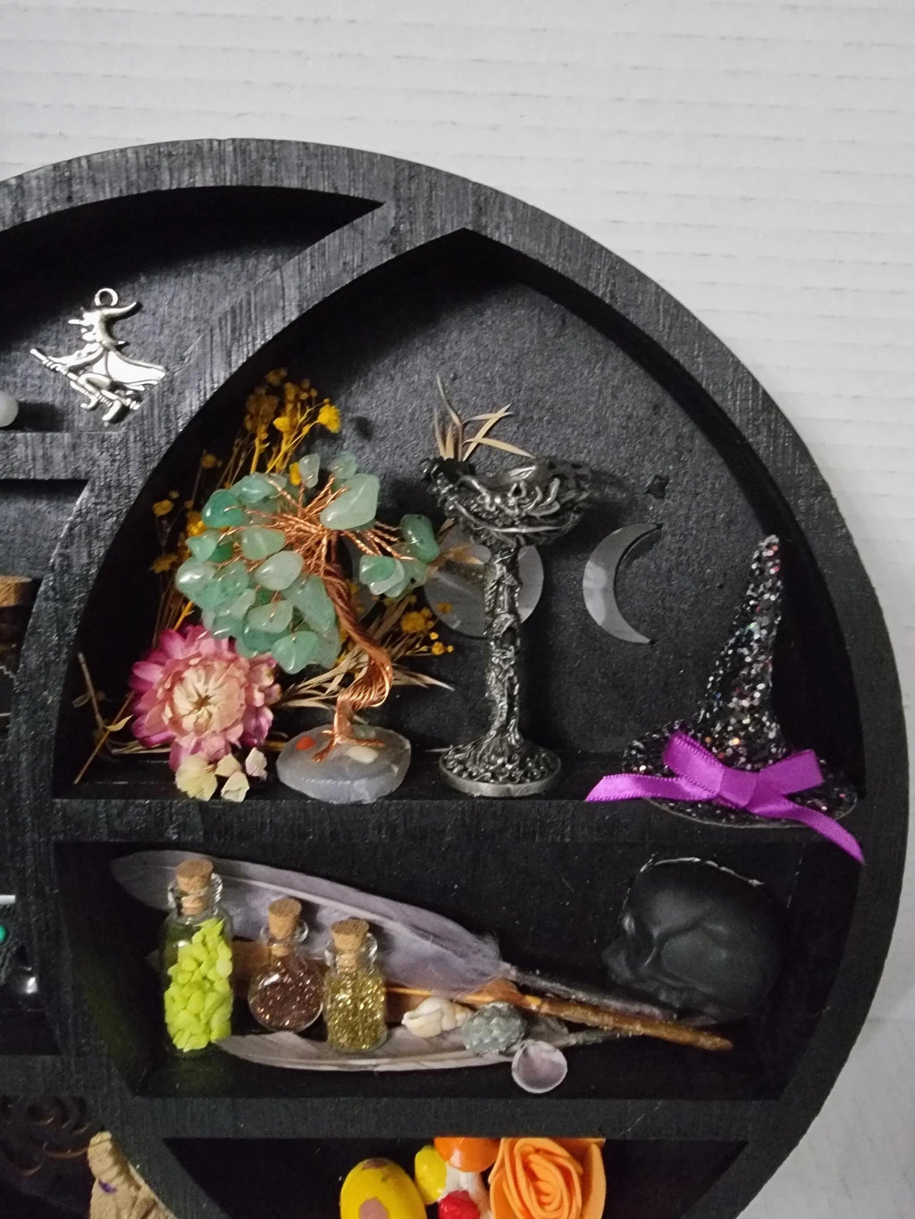 Decorative shelf with various small objects including flowers, bottles, and a purple bow on a gray background.