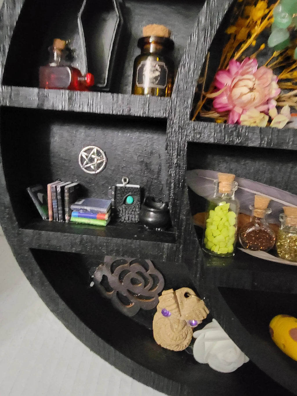 Black circular shelf with various items including bottles, books, and decorative objects.