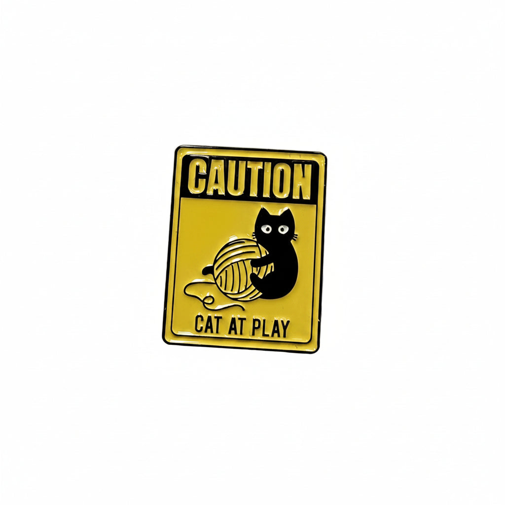 a yellow enamel pin with a cat playing and text on a white background