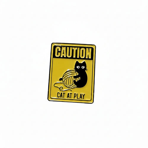 a yellow enamel pin with a cat playing and text on a white background