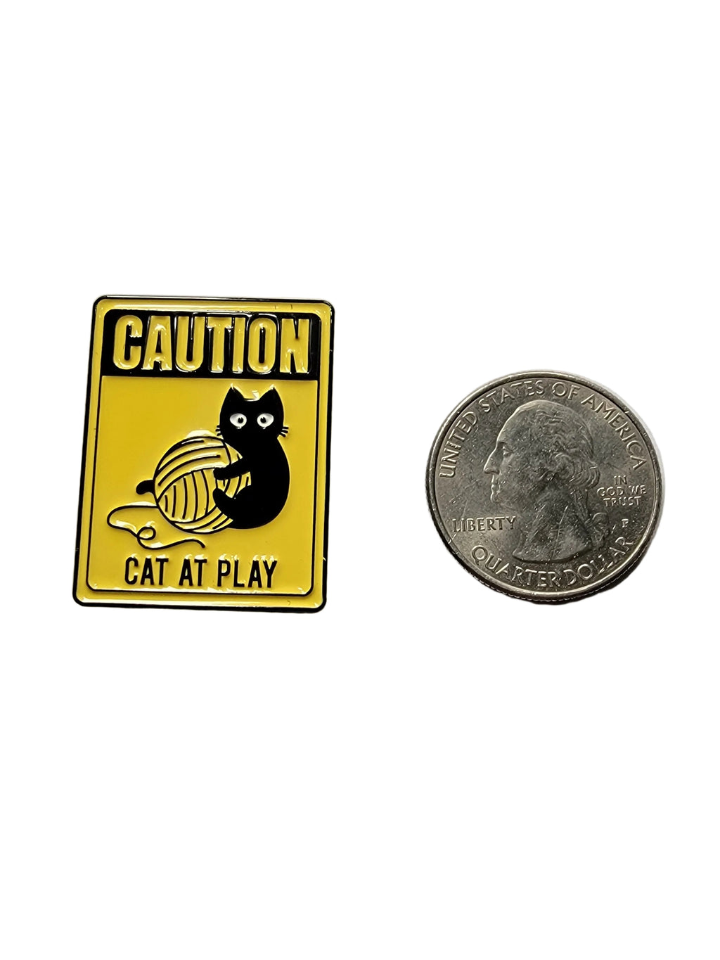 a yellow pin with a cat playing on it next to a quarter on a white background