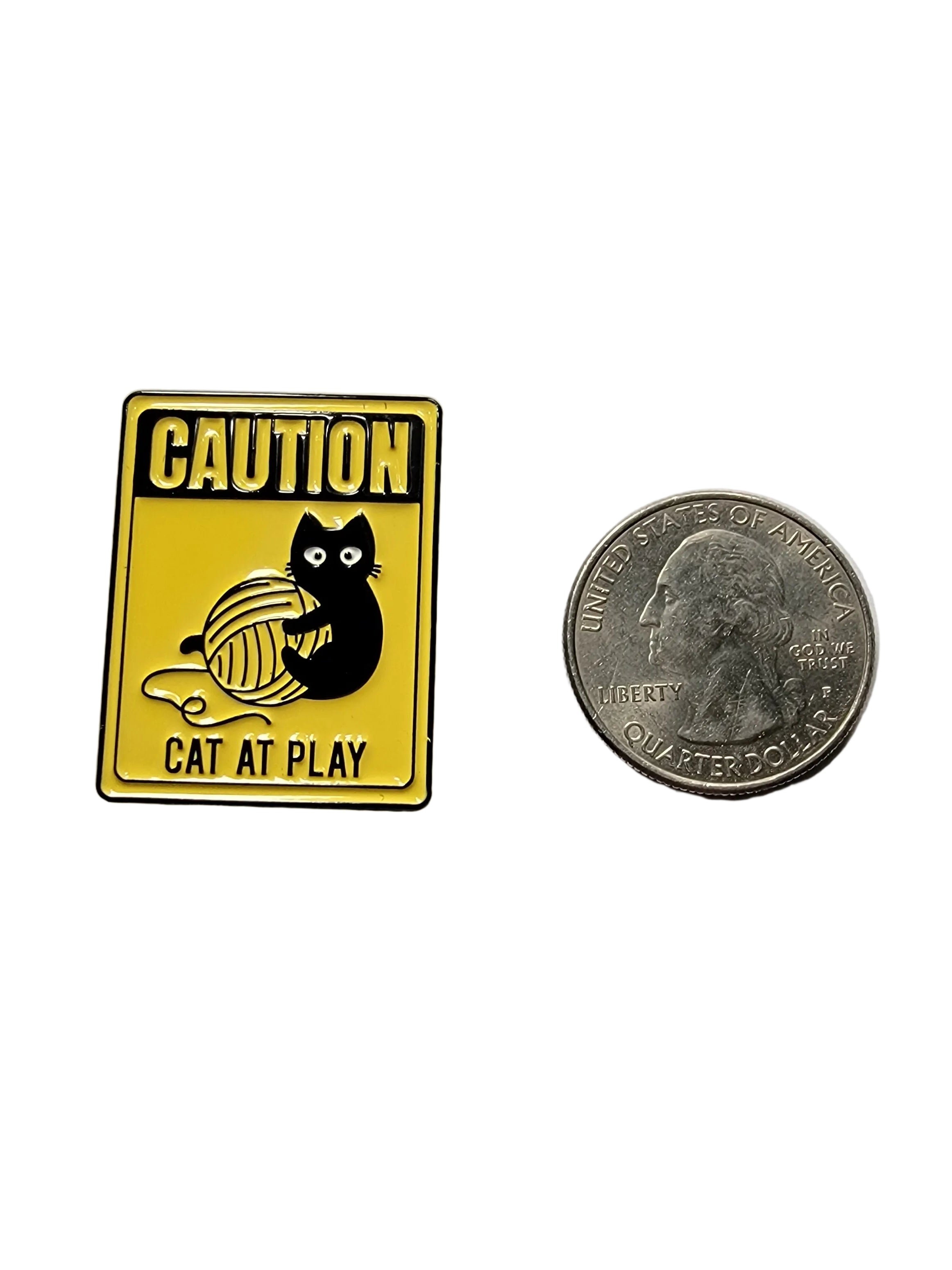 a yellow pin with a cat playing on it next to a quarter on a white background