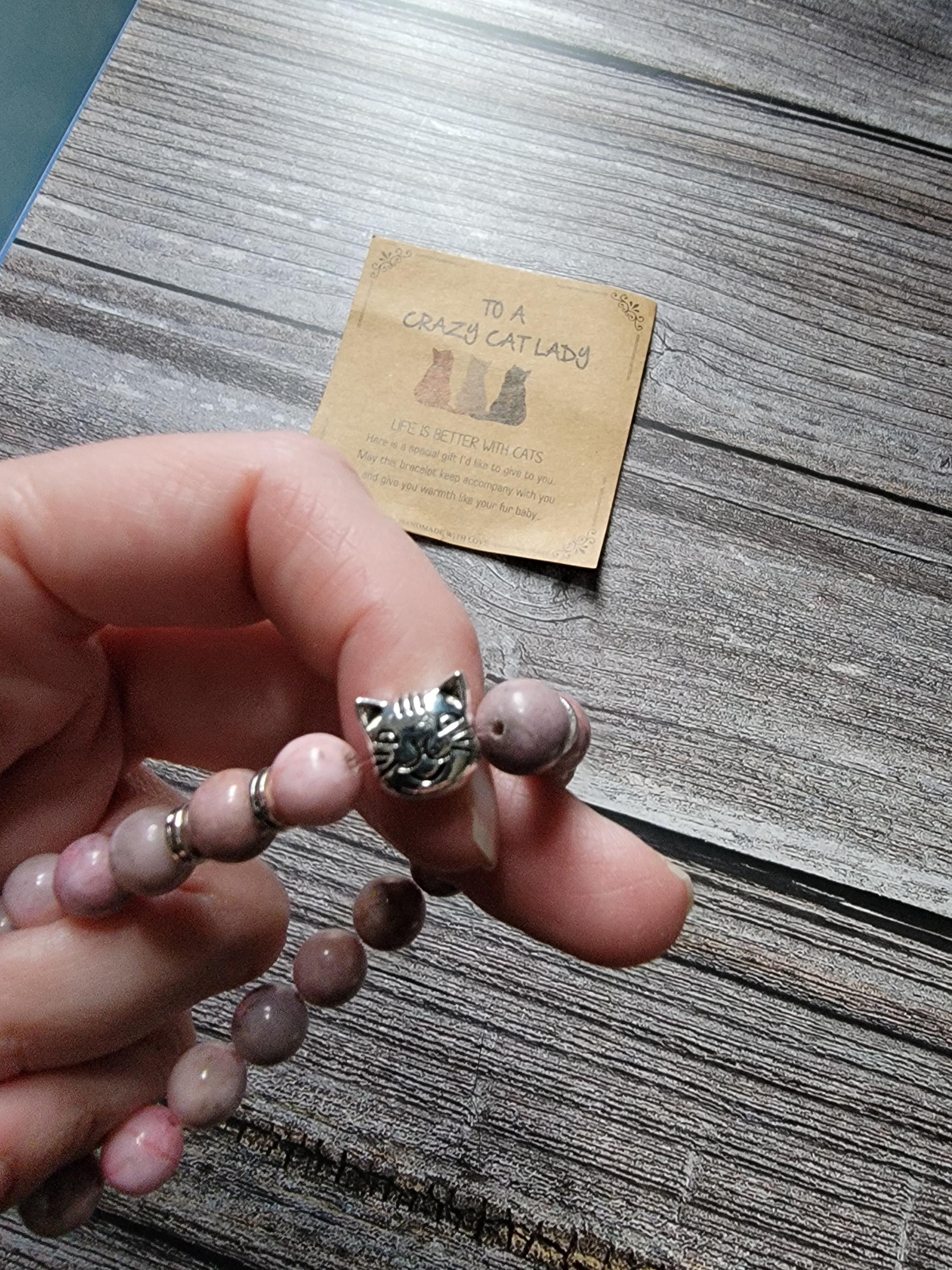 Hand holding a bracelet with cat-shaped beads on a wooden surface