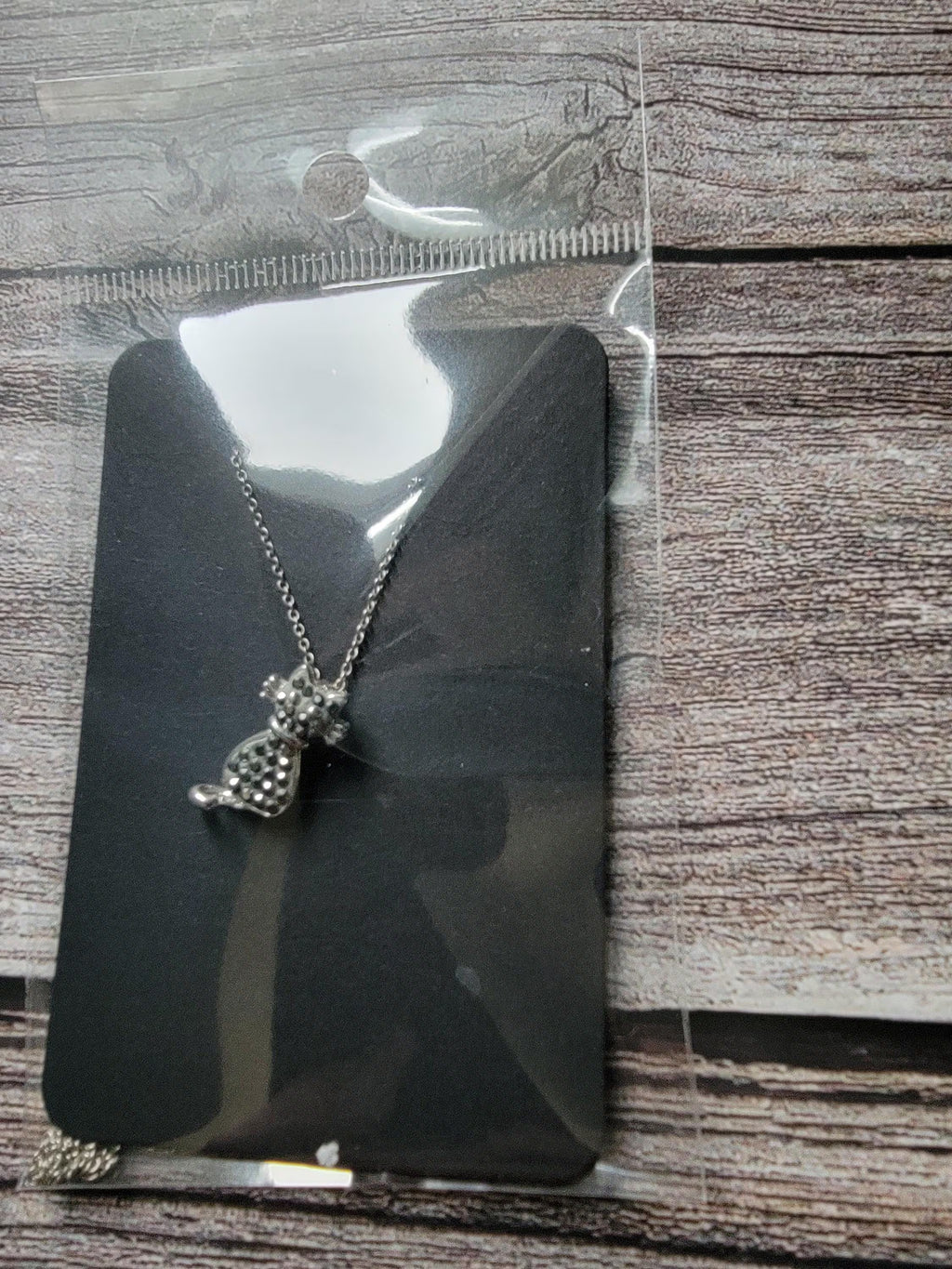 Butterfly-shaped necklace on a black card with a ruler for scale, on a wooden surface