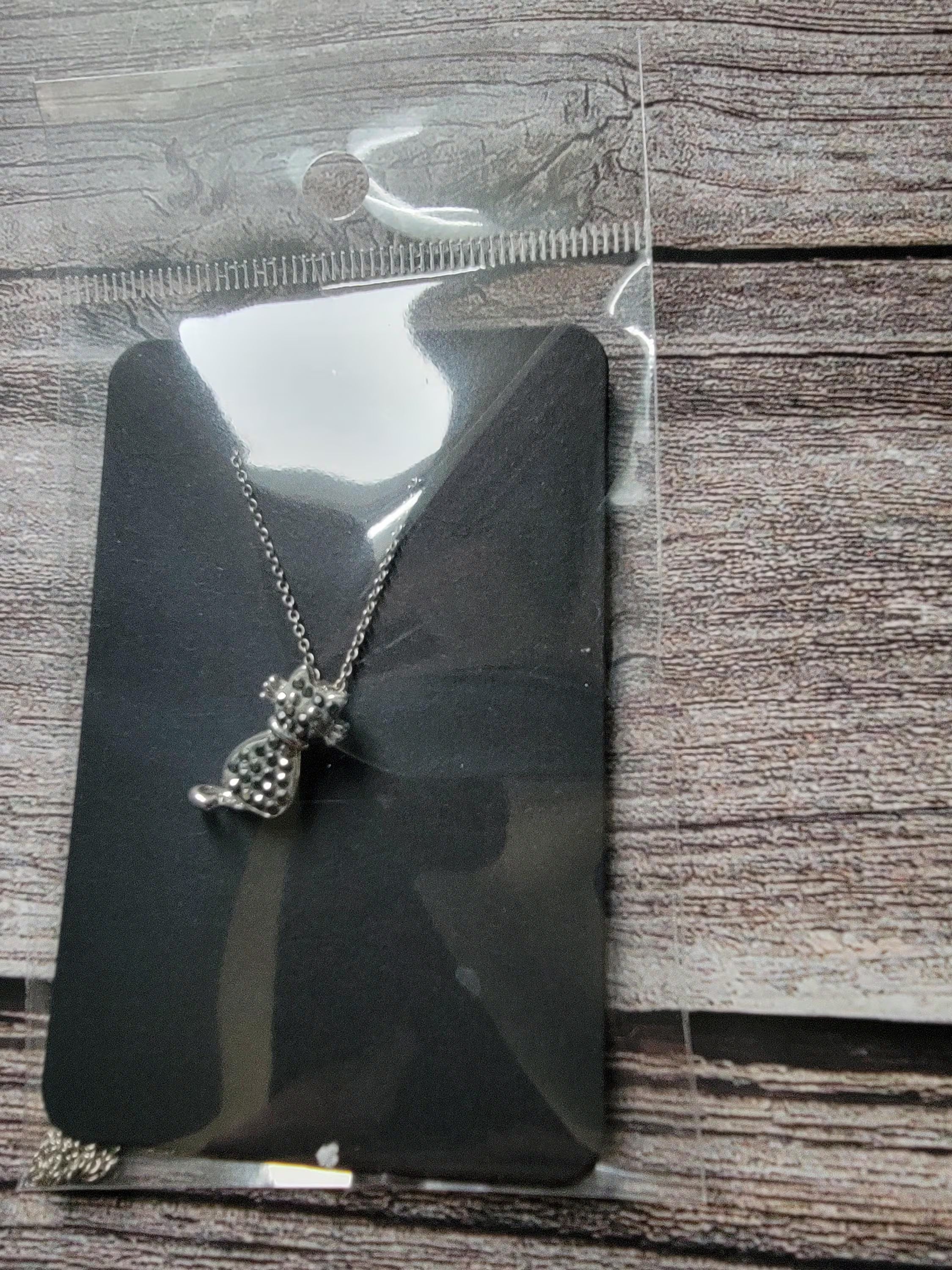 Butterfly-shaped necklace on a black card with a ruler for scale, on a wooden surface
