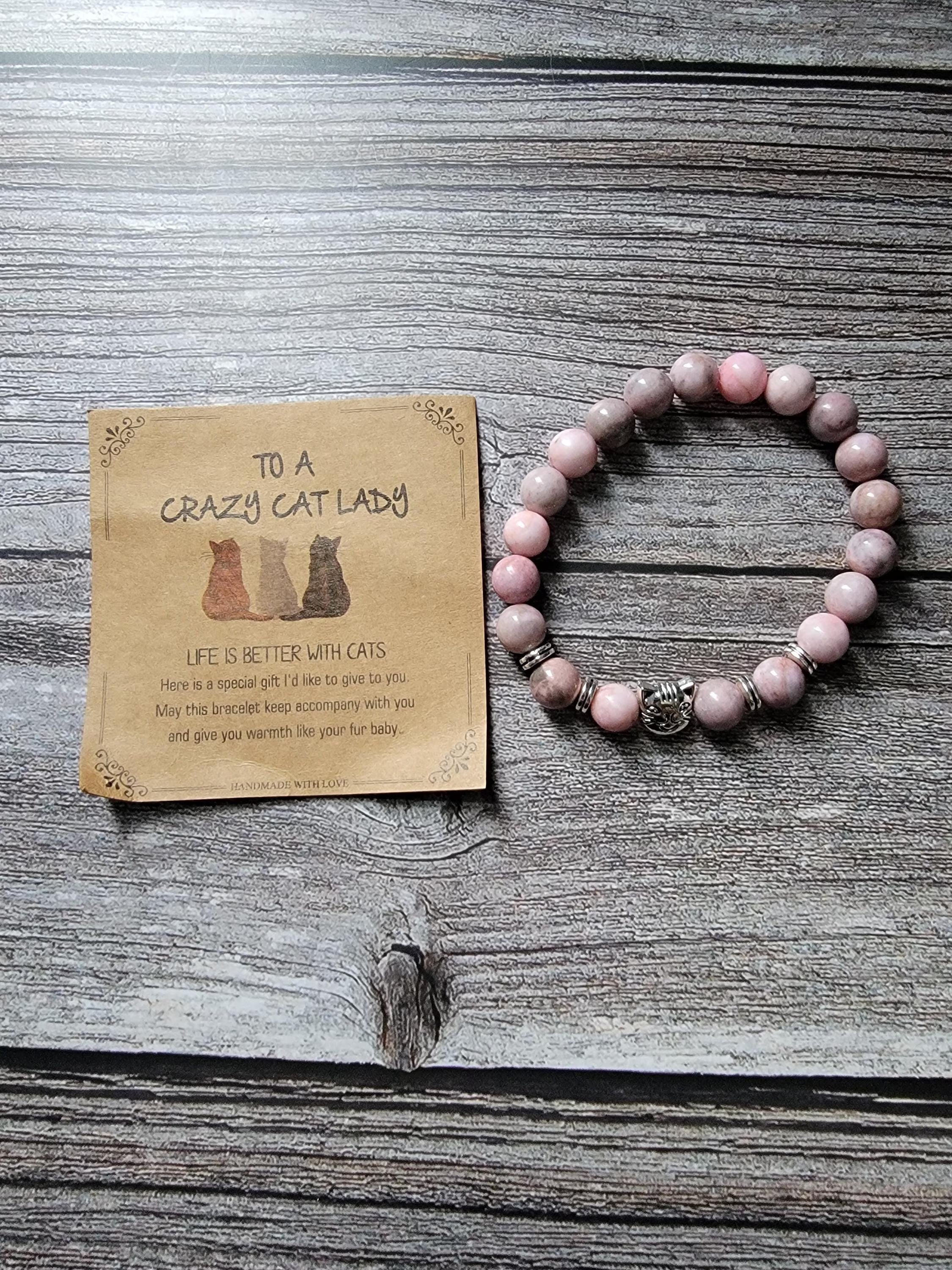Pink beaded bracelet on a wooden surface with a card reading 'To a crazy cat lady'.