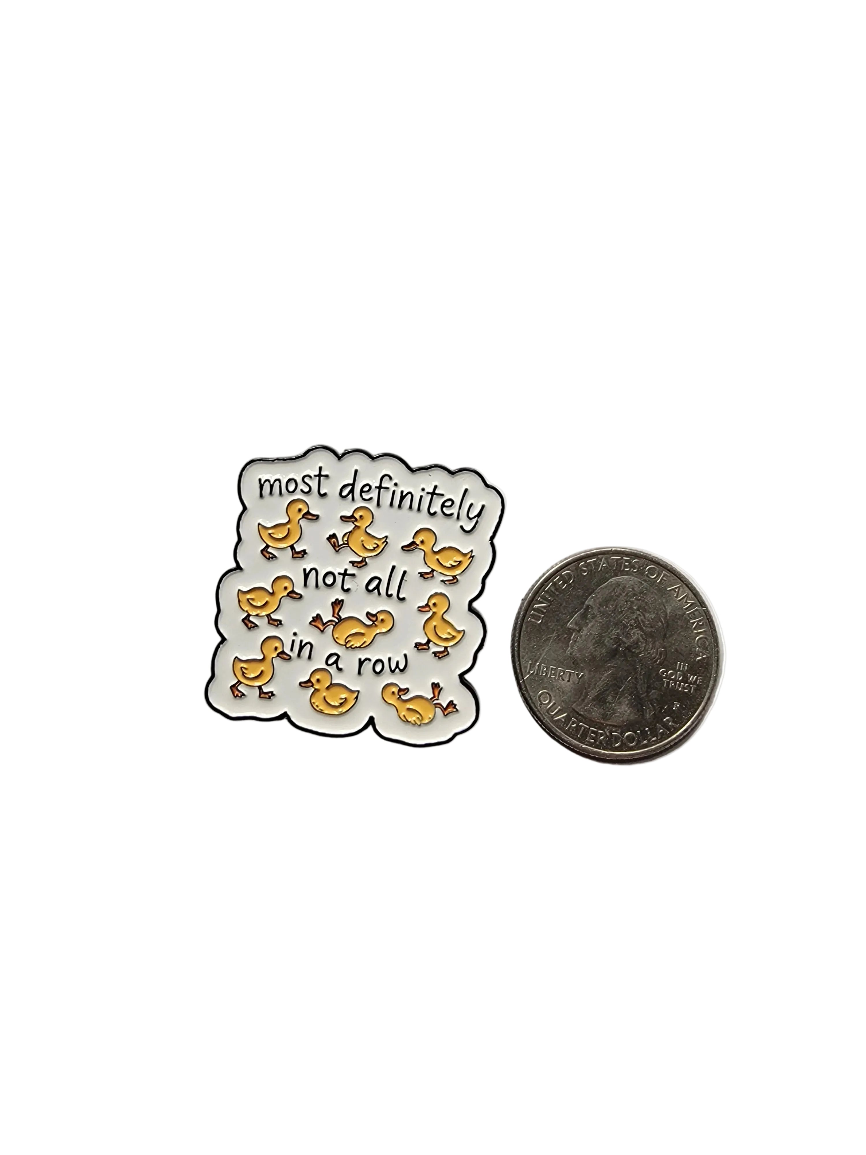 Pin with text and duck illustrations next to a quarter on a gray background