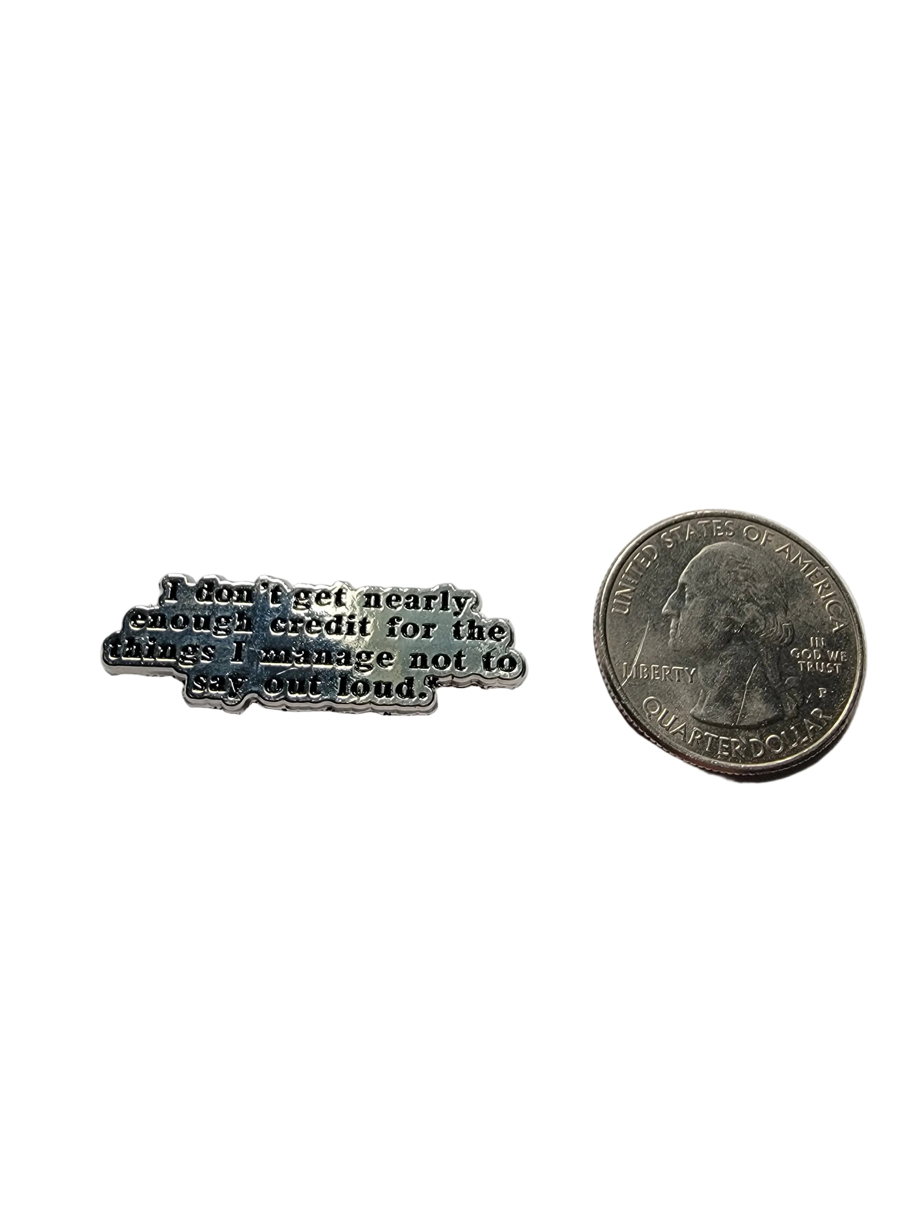 Small metal object with engraved text next to a quarter on a white background